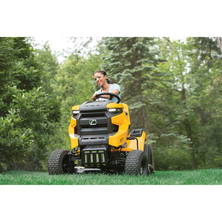 Person operating a yellow riding lawn mower in a grassy area with trees in the background
