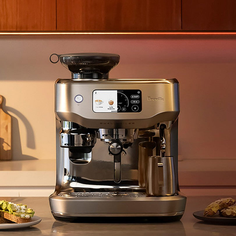 Stainless steel Breville coffee machine on a kitchen counter with wooden cabinets in the background.