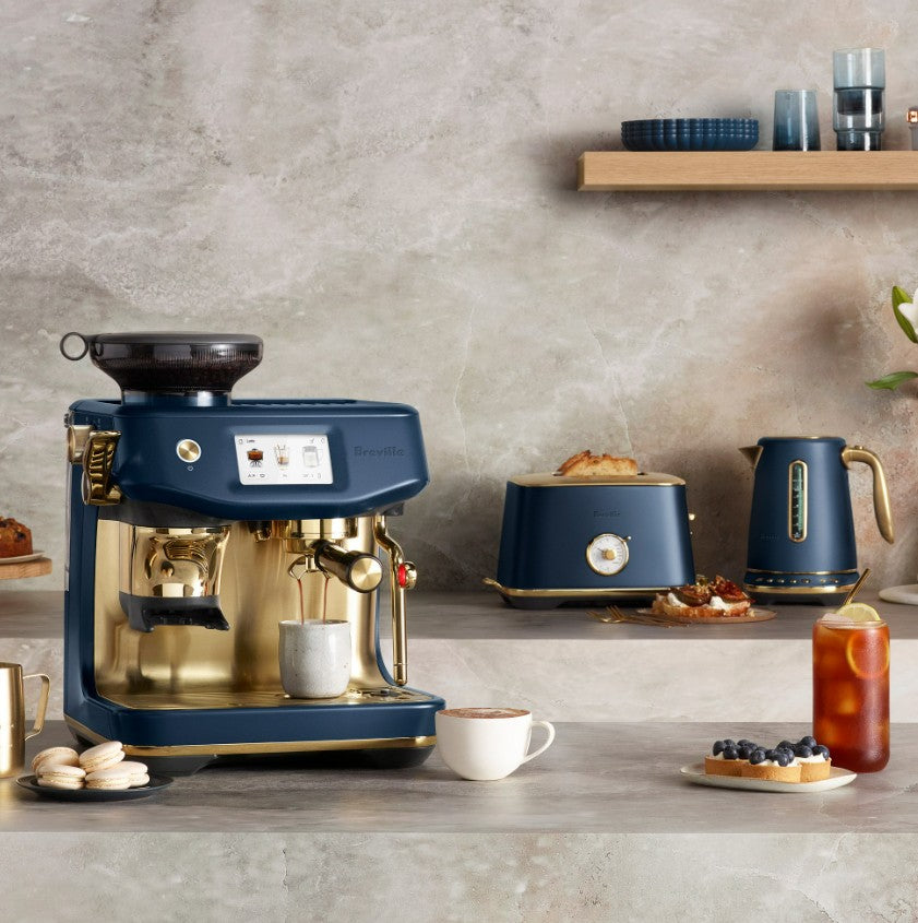 Blue and gold coffee machine on a kitchen counter with a toaster and kettle in the background.