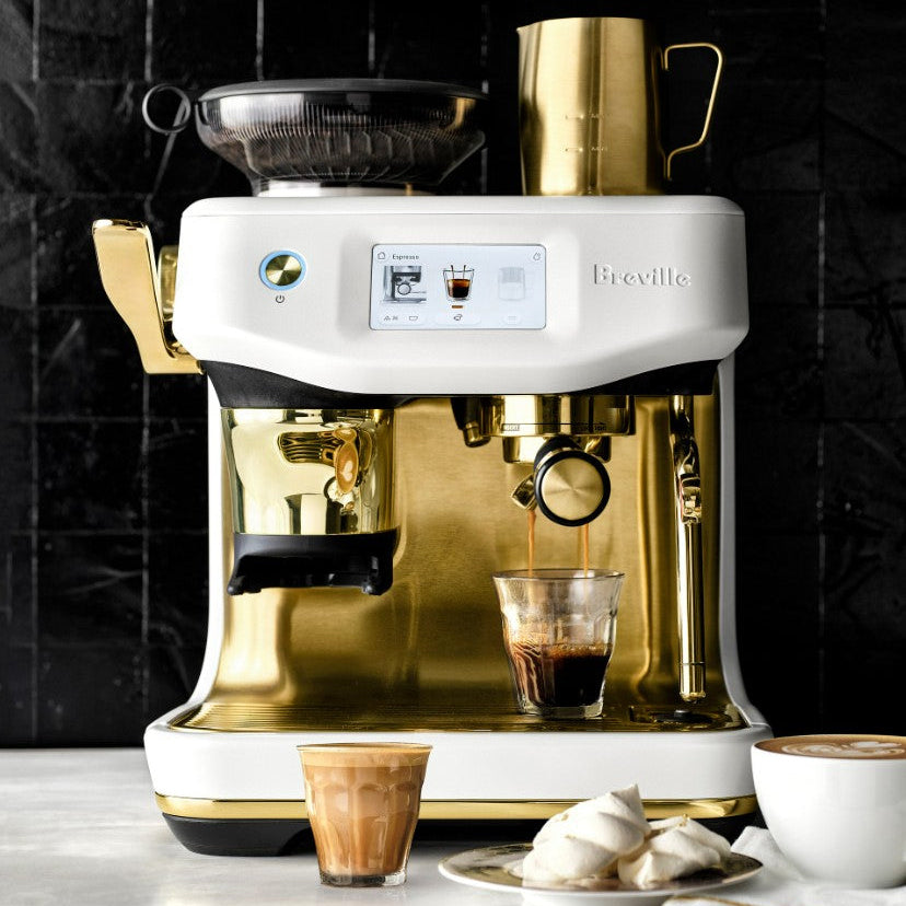 Breville coffee machine with a glass of coffee and a plate of cookies on a marble surface.