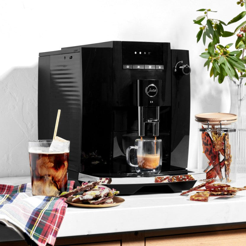 Black coffee machine on a kitchen counter with a cup of coffee and snacks.