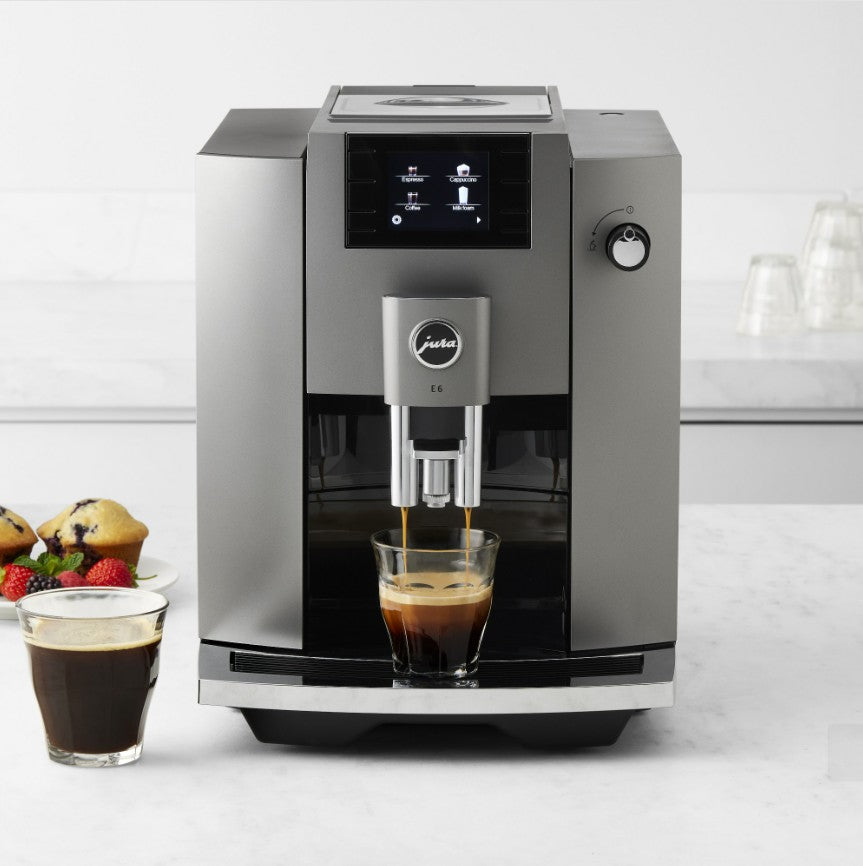 Modern coffee machine dispensing a cup of coffee on a kitchen counter with a glass of coffee and a plate of pastries.