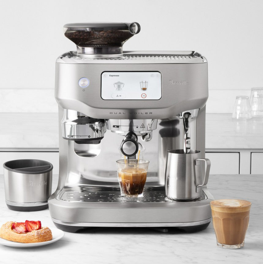 Breville coffee machine on a kitchen counter with a glass of coffee and a plate of pastries.