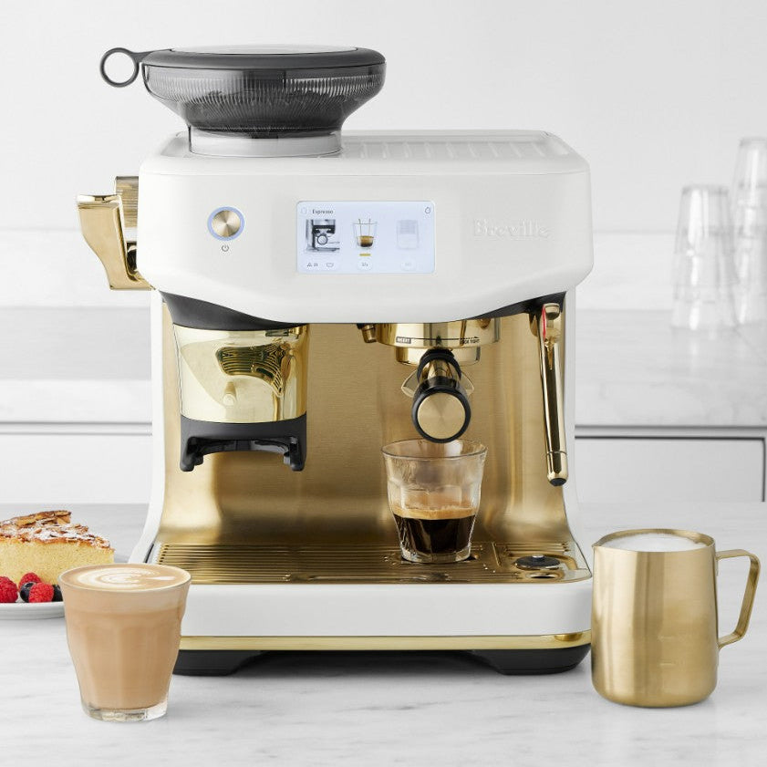 Gold and white espresso machine with a glass of coffee and milk on a light background