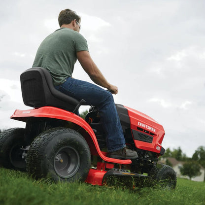 Man operating a red Craftsman riding lawn mower on grass with a cloudy sky.