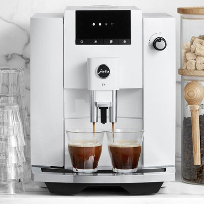 White coffee machine dispensing coffee into two glasses on a kitchen counter.