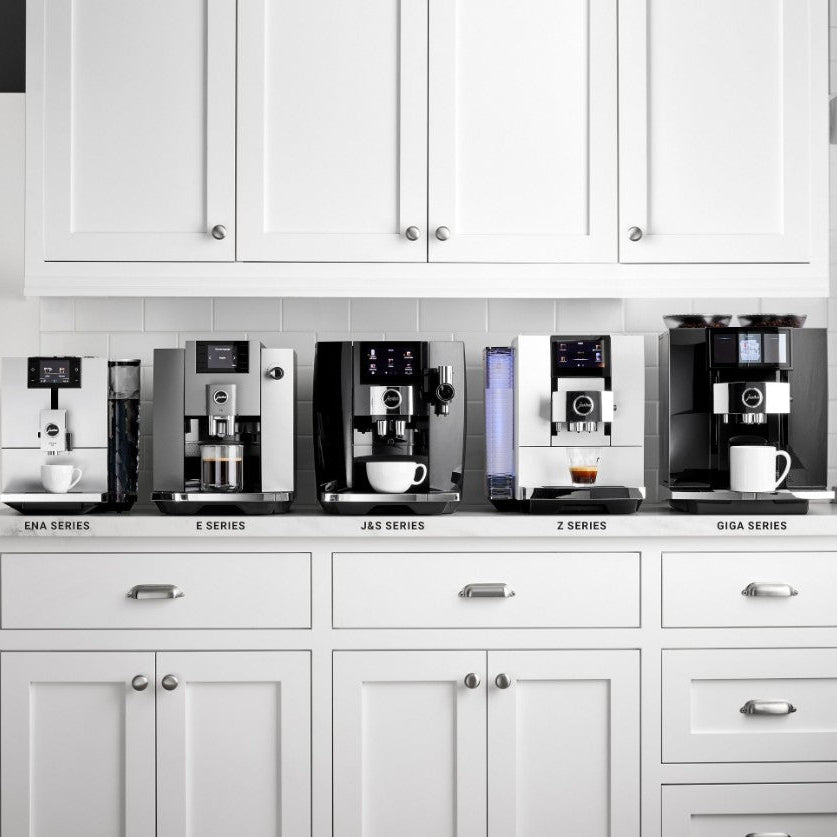 Row of coffee machines displayed against a white kitchen cabinet background