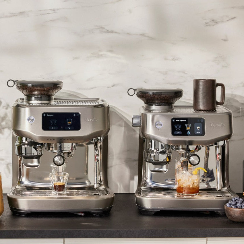 Two Breville espresso machines on a kitchen counter with drinks and ingredients.