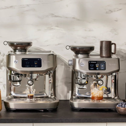 Two Breville espresso machines on a kitchen counter with drinks and ingredients.