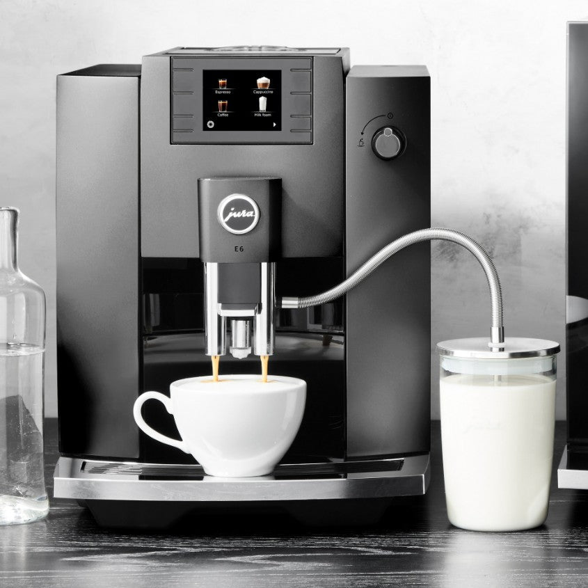 Jura coffee machine brewing a cup of coffee with a glass of milk on a wooden surface.