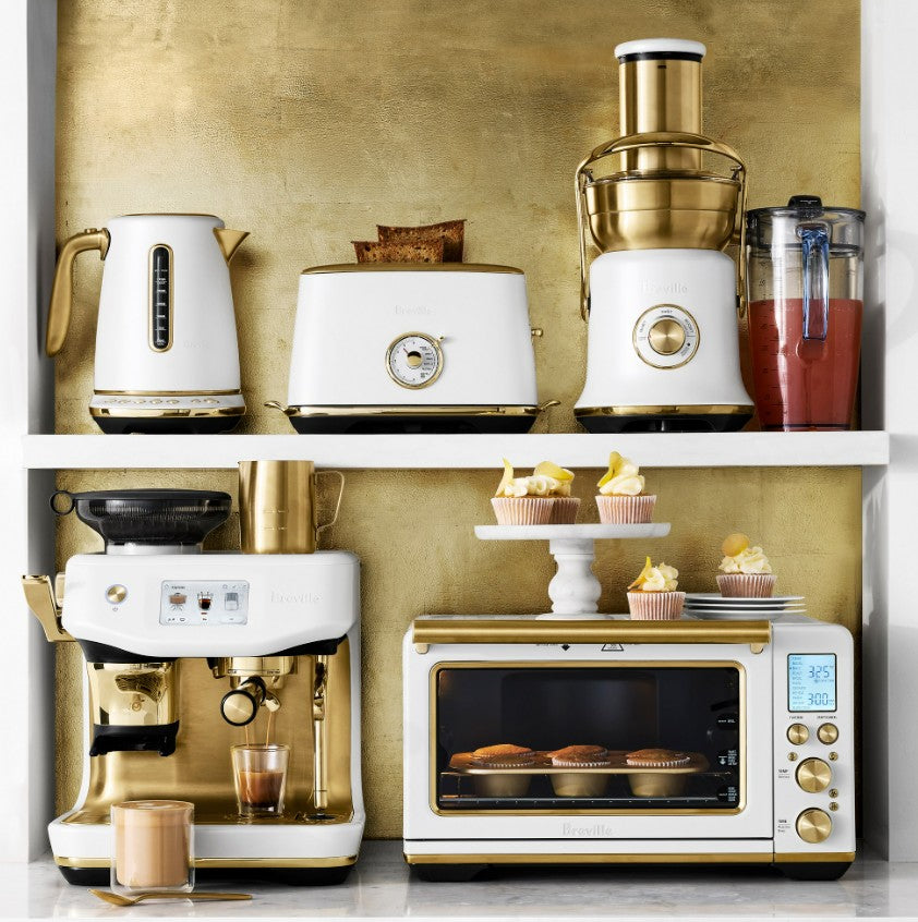 Kitchen appliances including a coffee machine, toaster, blender, and oven on a shelf with a gold wall background.