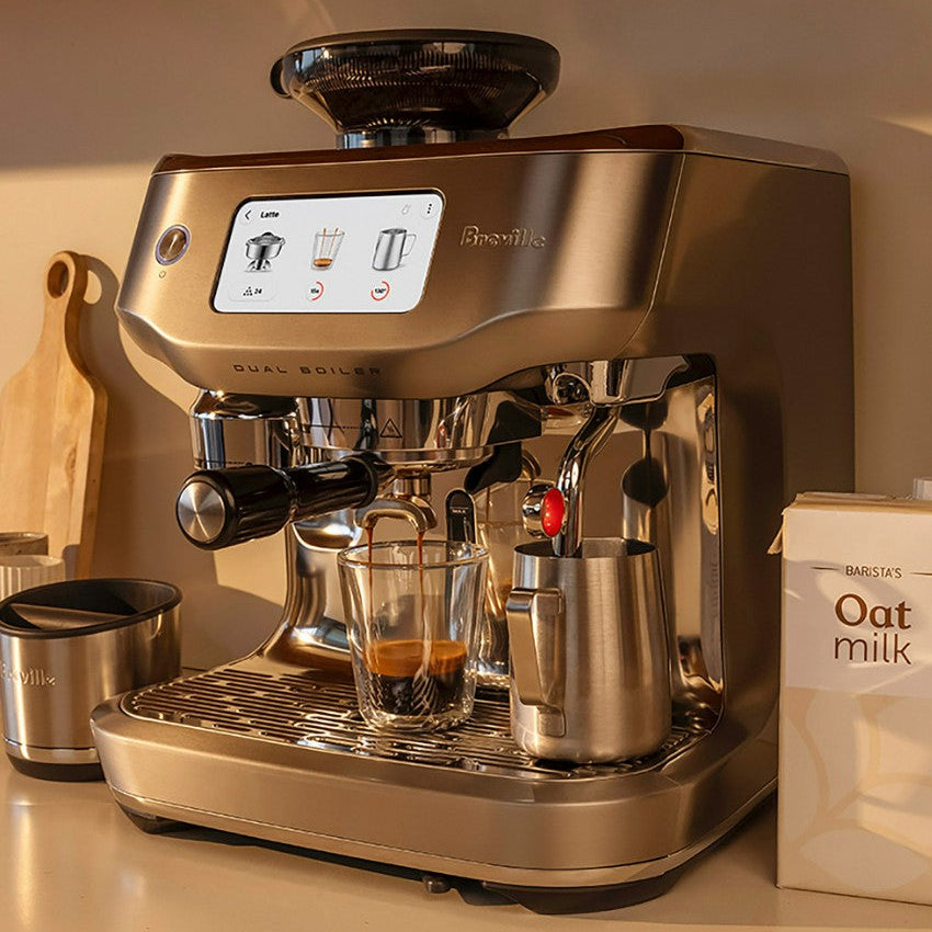 Breville coffee machine with a glass of coffee and a carton of oat milk on a countertop.