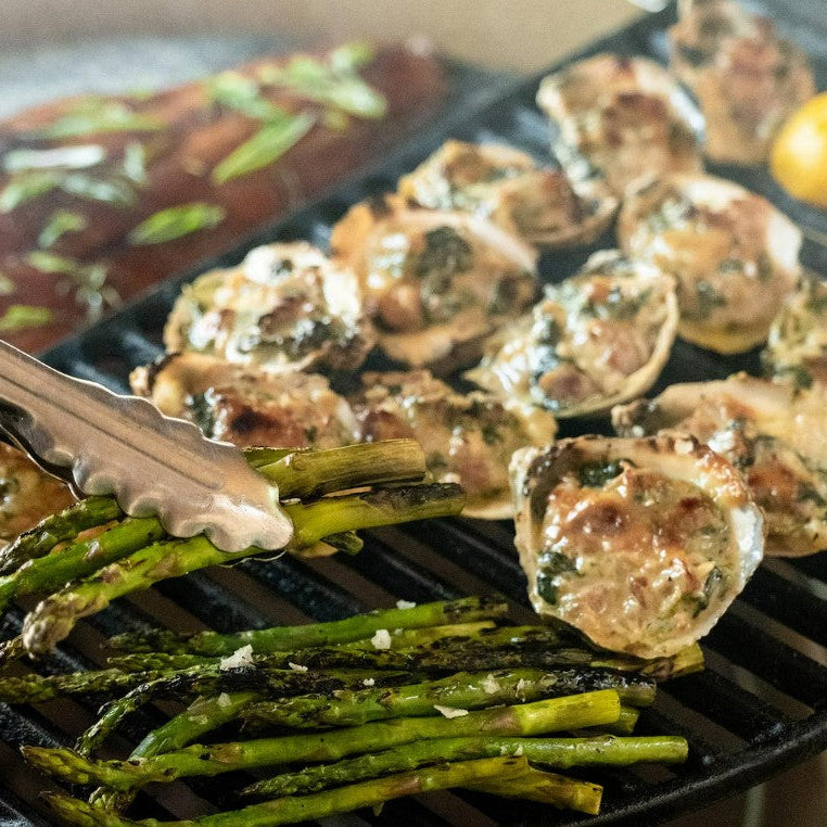 Grilled asparagus and stuffed mushrooms on a grill pan with tongs.