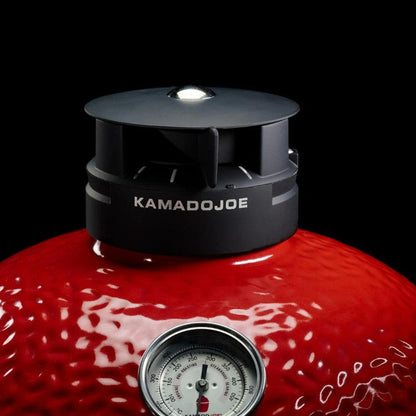 Red Kamado Joe grill with a black lid and thermometer on a black background