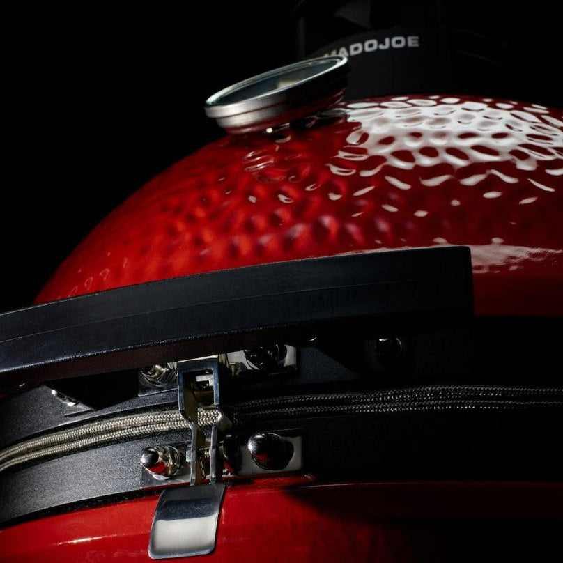 Close-up of a red barbecue grill with a lid, featuring a brand name in the background.
