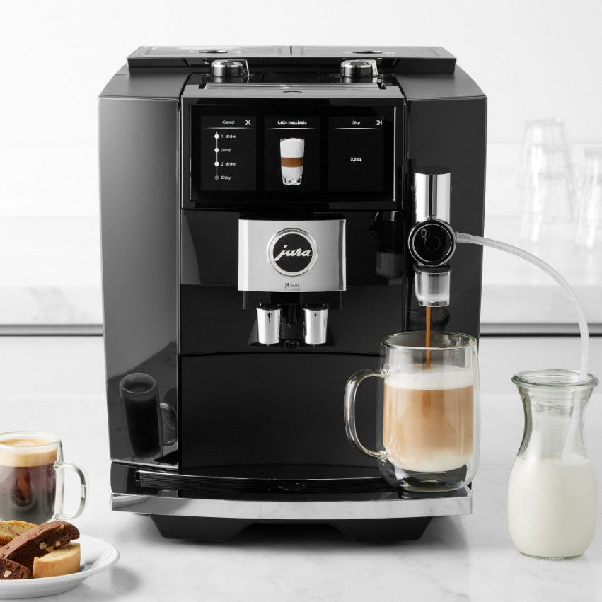 Black coffee machine making a cup of coffee on a white surface with milk and cookies.