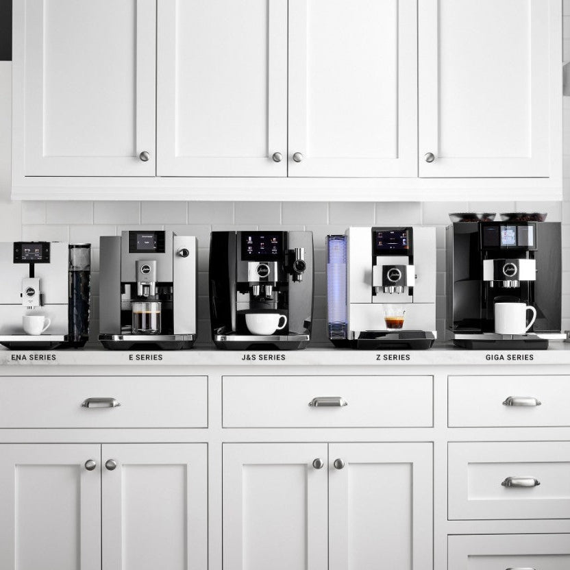 Row of coffee machines labeled with different series in a kitchen setting.