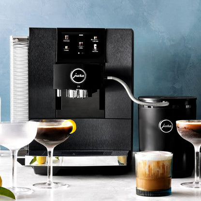 Black coffee machine with Jura logo on a table with glasses of coffee and a cup.