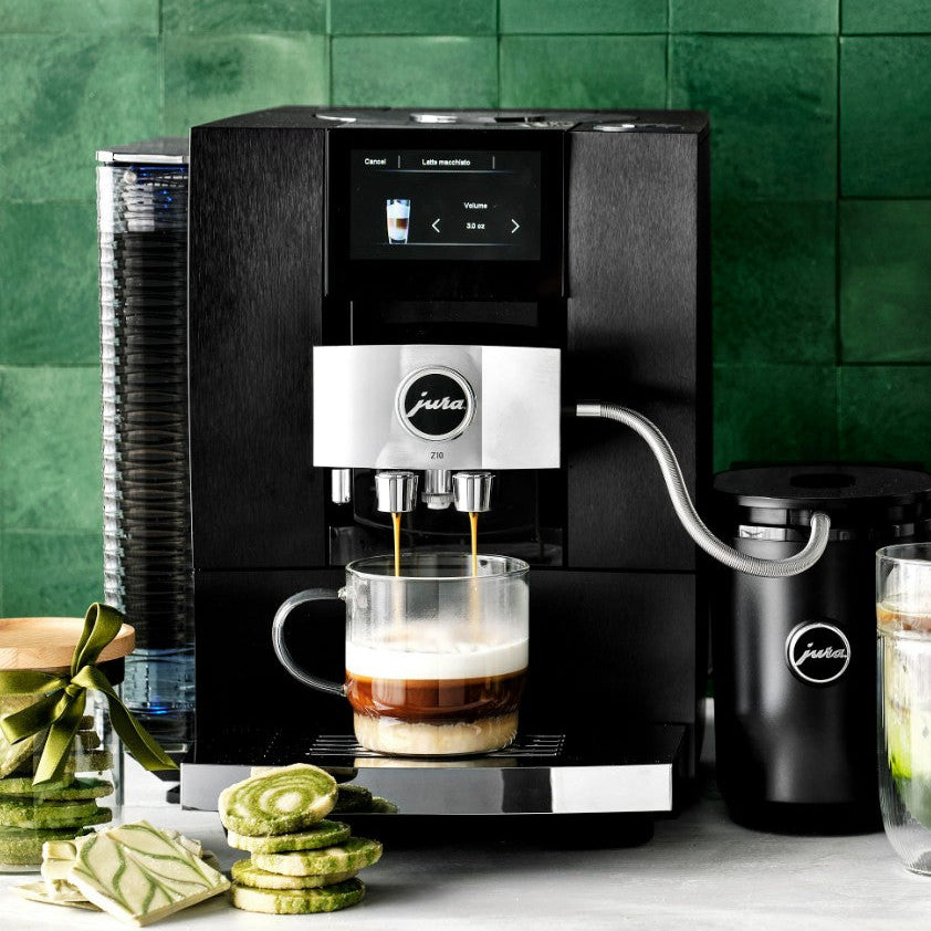 Black coffee machine brewing a cup of coffee with a green tiled wall in the background