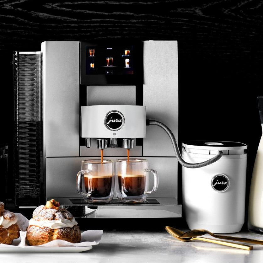 Jura coffee machine with two cups of coffee and pastries on a dark background
