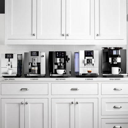 Row of coffee machines on a kitchen counter with white cabinets.