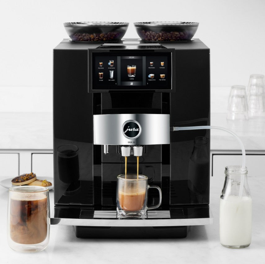 Black coffee machine making a cup of coffee with ingredients around on a white countertop.