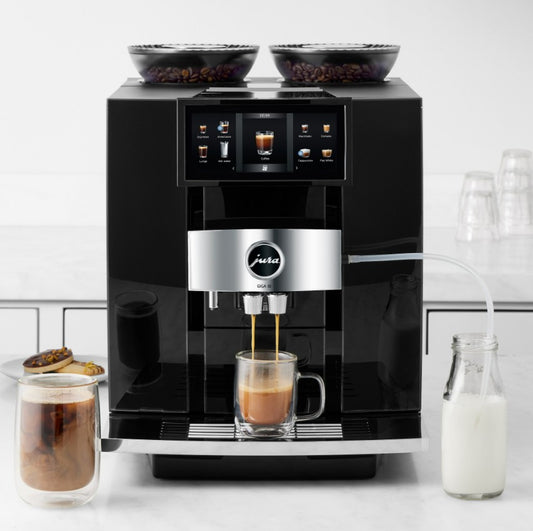 Black coffee machine making a cup of coffee with ingredients around on a white countertop.