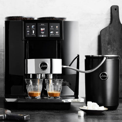 Black and silver coffee machine with two glasses of coffee on a wooden surface.
