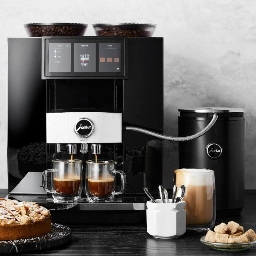 Coffee machine with two cups of coffee, a kettle, and a cake on a wooden table.