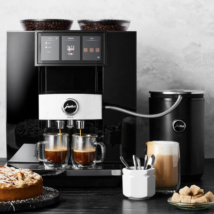 Coffee machine with two cups of coffee, a kettle, and a cake on a wooden table.