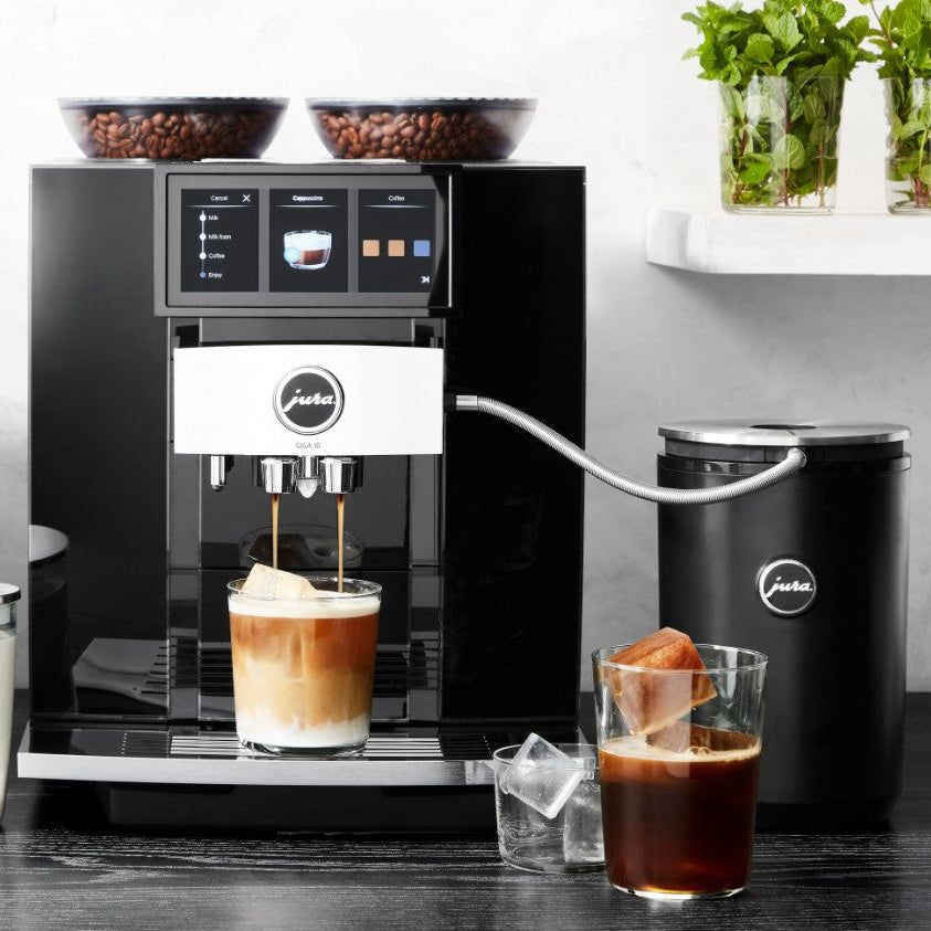 Jura coffee machine dispensing a drink with a glass of iced coffee and a cup of coffee on a wooden surface.
