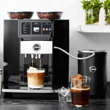 Jura coffee machine dispensing a drink with a glass of iced coffee and a cup of coffee on a wooden surface.