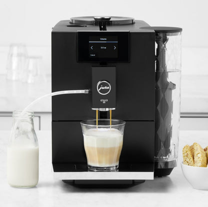 Black coffee machine making a latte with a glass of milk and cookies on a white surface