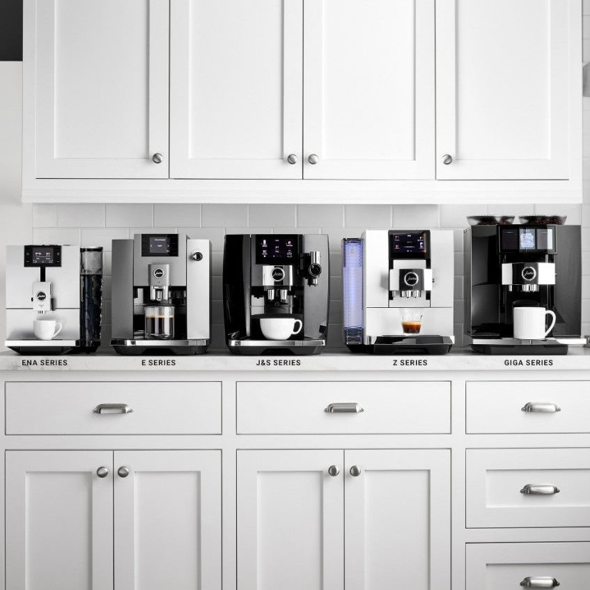 Row of coffee machines on a kitchen counter with white cabinets.